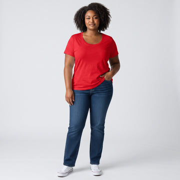 A woman modeling a bright red short-sleeve scoop-neck t-shirt and dark blue jeans, standing against a light gray studio background.