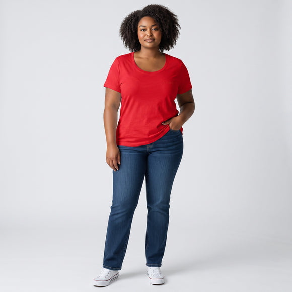 A woman modeling a bright red short-sleeve scoop-neck t-shirt and dark blue jeans, standing against a light gray studio background.