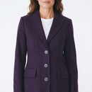 A woman wearing a dark purple wool-blend blazer with notched lapels and three front buttons, styled over a white crewneck top against a plain white background.