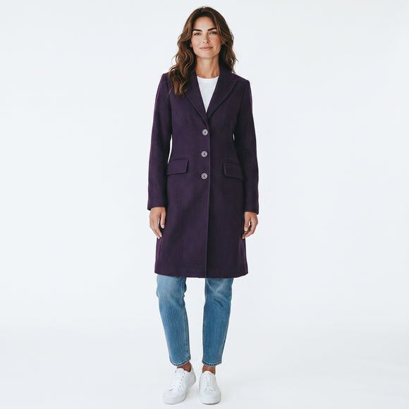 A woman modeling a dark purple knee-length coat with three front buttons, worn over a white top and blue jeans, against a plain white studio background.