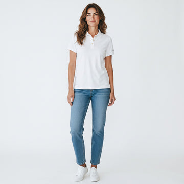 A woman modeling a white short-sleeve polo shirt with light blue jeans and white sneakers, standing against a plain white studio background.