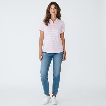 A woman modeling a light pink and white striped short-sleeve polo shirt with blue jeans and white sneakers, standing against a plain white studio background.