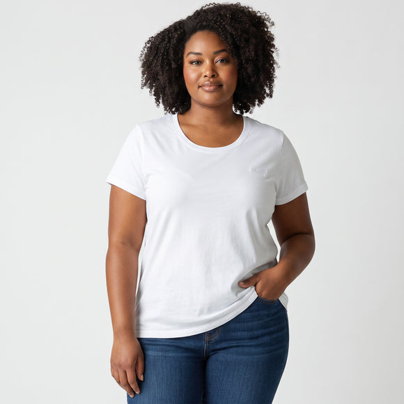 A woman with curly dark hair wearing a plain white short-sleeve crewneck t-shirt and blue jeans, standing against a light gray studio background.